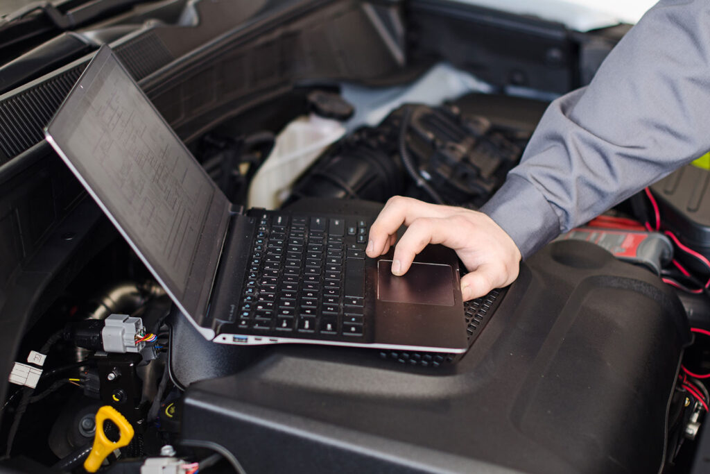 A technician performs a diagnostic test on a car engine using a laptop.